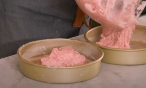 Pink batter is carefully poured into a prepared cake pan