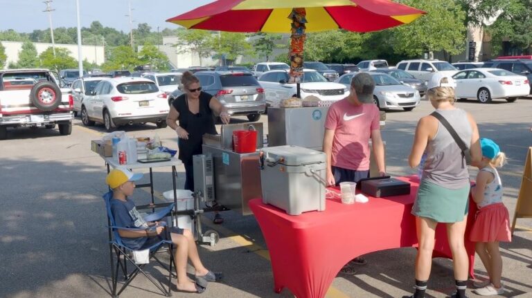 A food truck operates in a parking lot, offering various treats to passersby