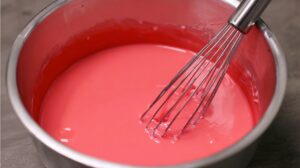 A mixing bowl filled with smooth, bright pink Kool-Aid pie filling being whisked with a metal whisk