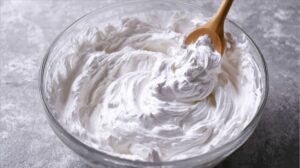 A glass bowl filled with fluffy white whipped topping being stirred with a wooden spoon