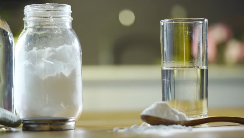 Baking soda in a jar next to a glass of water and a spoon with baking soda
