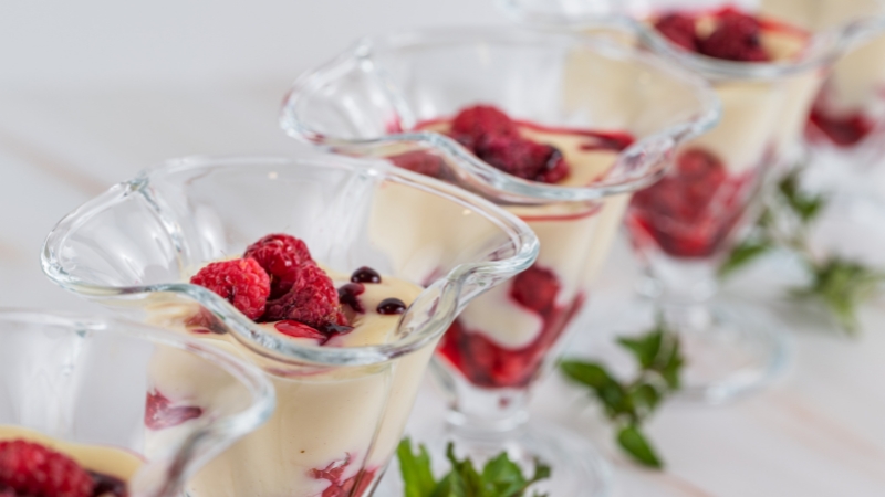 Clear dessert glasses filled with creamy layers and fresh raspberries, arranged neatly in a row