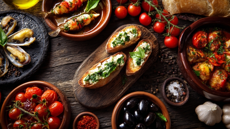 A table with fresh bruschetta, olives, tomatoes, stuffed peppers, and mussels served as part of a traditional Italian appetizer spread