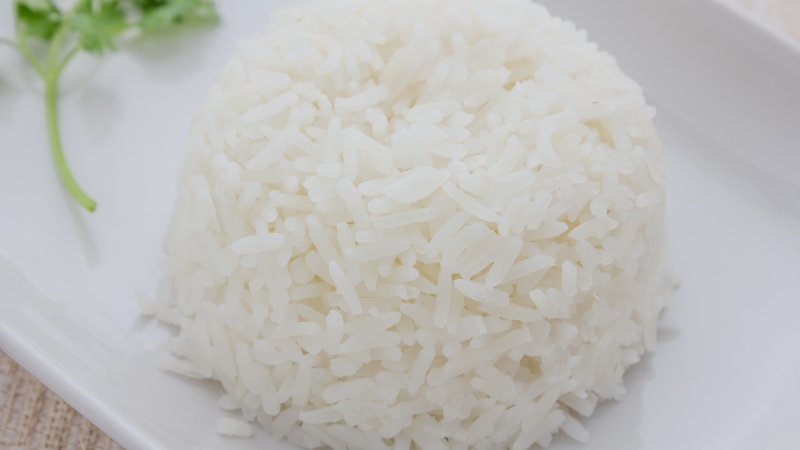A portion of freshly cooked white rice served on a plate with a parsley garnish in the corner