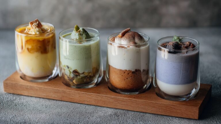 Dessert glassware with layered treats in clear cups, featuring colorful smoothies, cakes, and ice cream served on a wooden tray