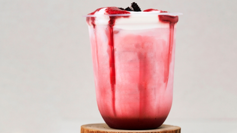 A plastic dessert glass filled with layered yogurt and berry sauce, topped with fruit and cookie pieces