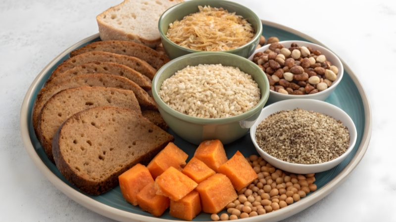 A plate with bread, grains, beans, nuts, and sweet potatoes shows foods too high in fiber