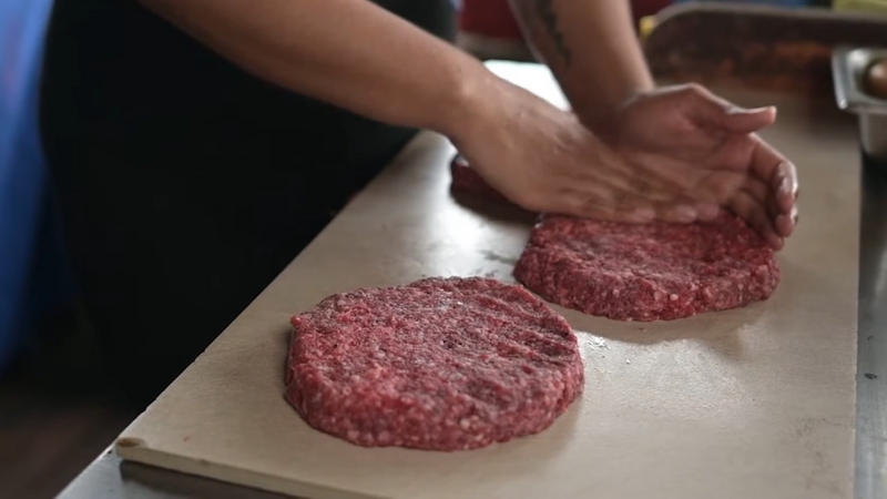 Ground beef patties being shaped by hand on a cutting board