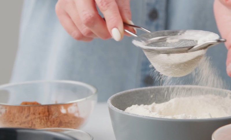A person is mixing baking powder into a bowl with a wooden spoon