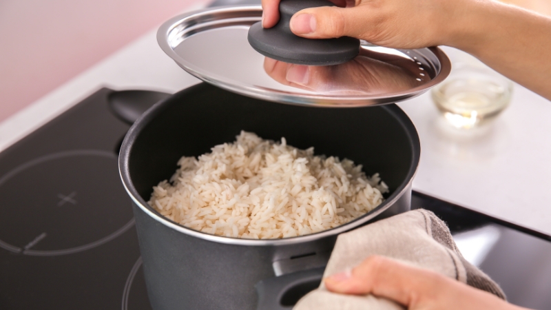 A pot of freshly cooked rice being uncovered on a stovetop