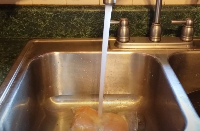 Chicken breast is being thawed under a stream of cool running water