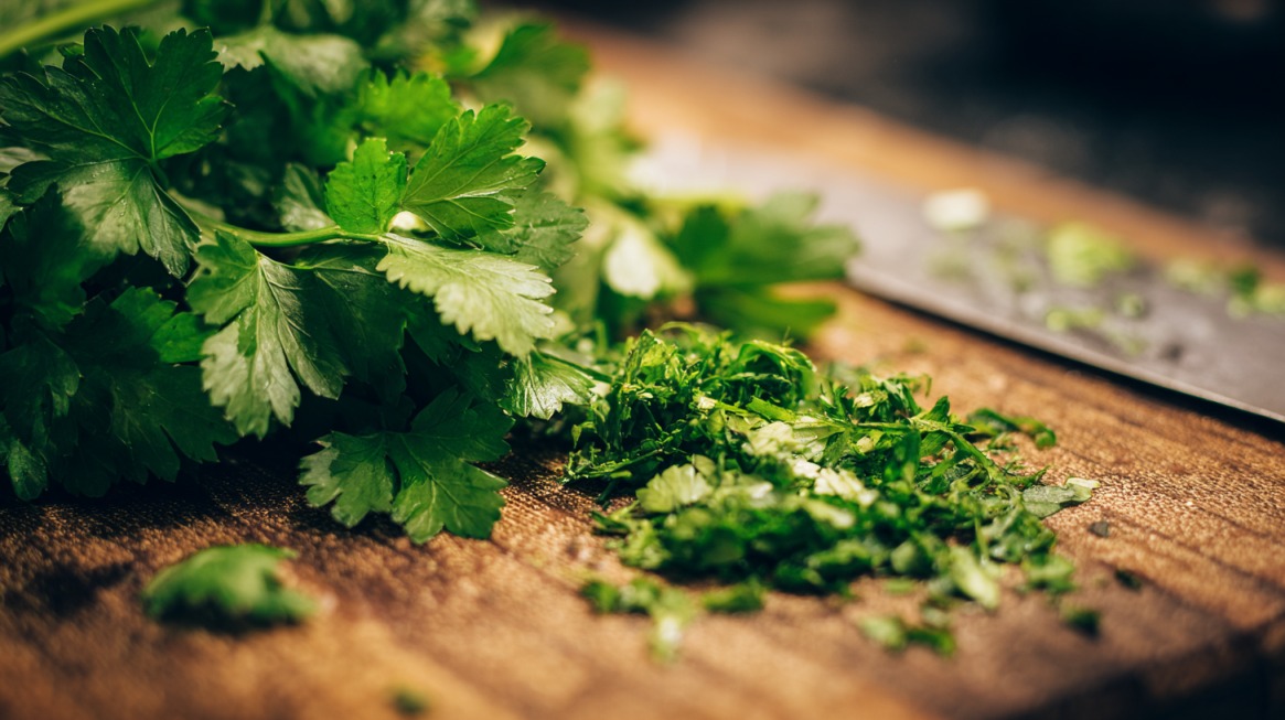 Close-up of fresh parsley being chopped on a wooden cutting board with a knife in the background