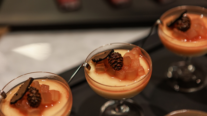 Elegant dessert glassware filled with creamy custard, topped with diced fruit, syrup, and a small garnish