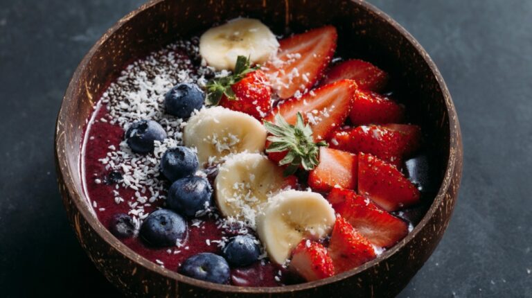 A colorful açaí bowl topped with sliced bananas, strawberries, blueberries, shredded coconut, and chia seeds