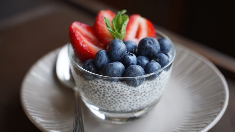 A glass bowl of chia seed pudding topped with fresh blueberries, sliced strawberries, and a mint leaf on a white plate
