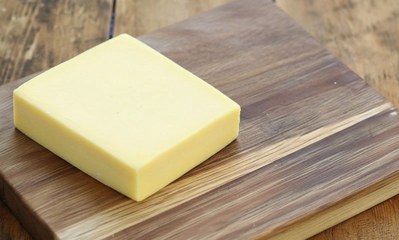 A square of cheddar cheese on a wooden cutting board