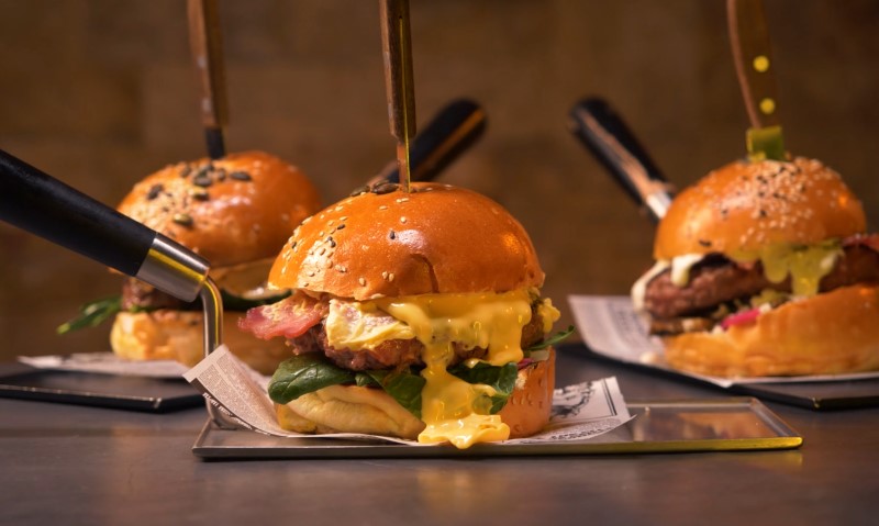 Three gourmet burgers, stacked high with bacon and dripping cheddar cheese