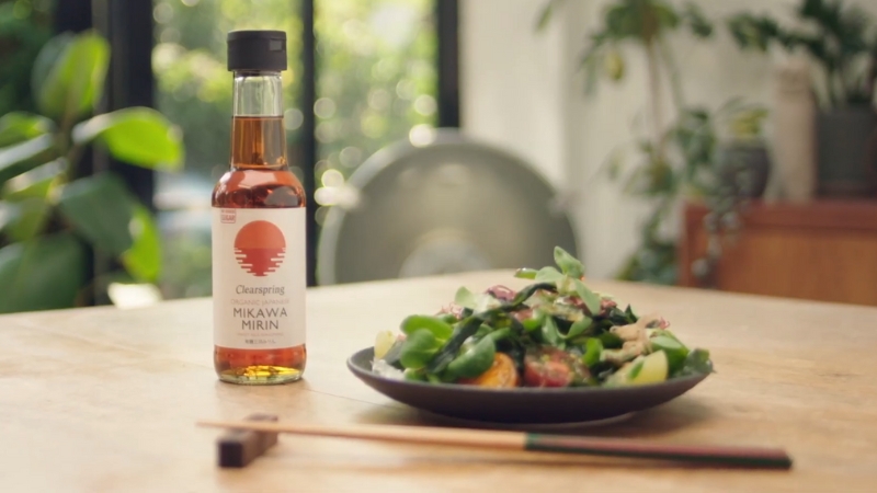 A bottle of mirin stands beside a plate of fresh Japanese salad on a wooden table