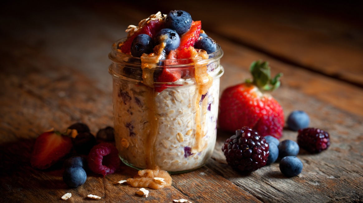 Jar of overnight oats with blueberries, strawberries, and peanut butter on a rustic wooden table