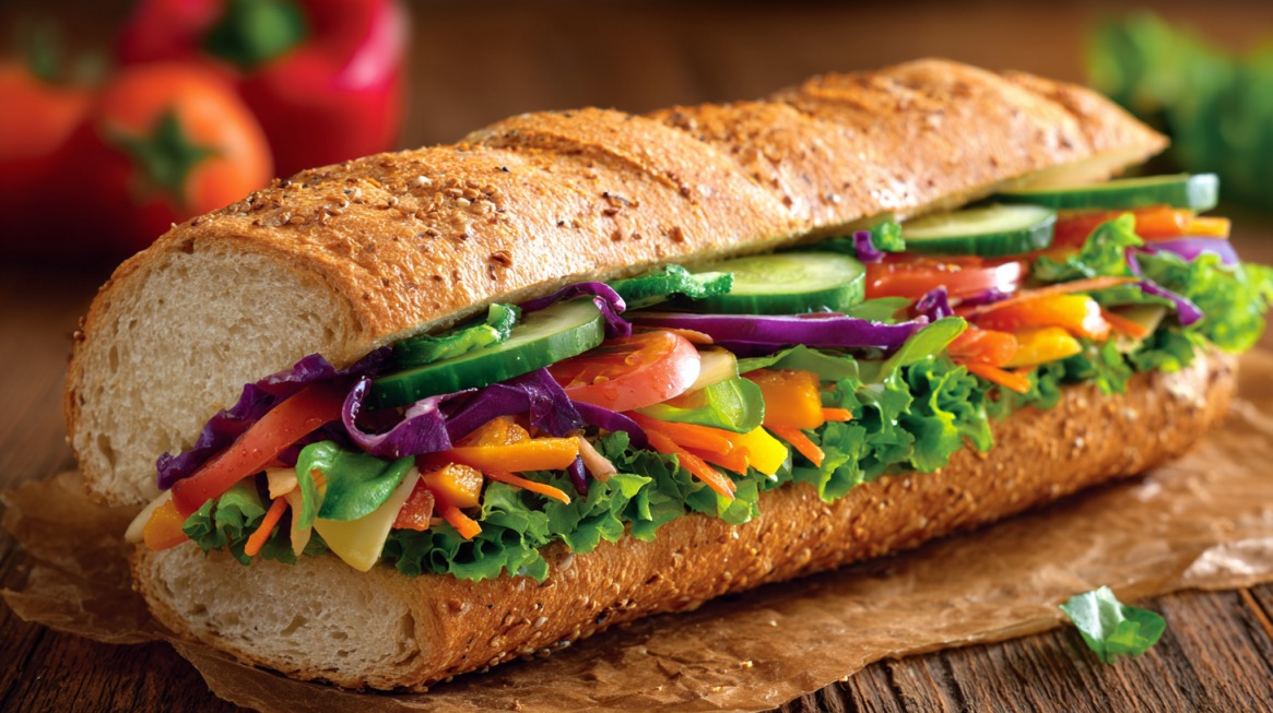 Close-up of a Subway Veggie Delite sandwich with lettuce, tomatoes, cucumbers, peppers, carrots, and purple cabbage on multigrain bread