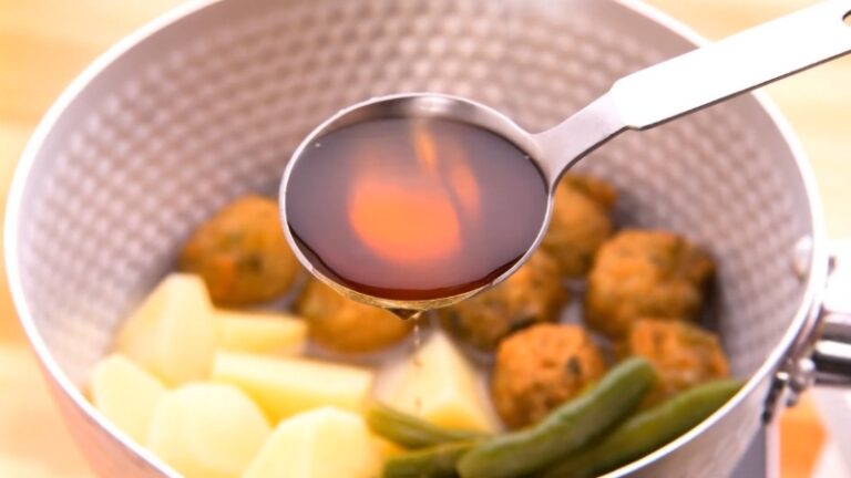 A spoonful of mirin being added to simmered vegetables and meatballs in a Japanese cooking pot