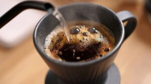Close-up of hot water being poured into a mug of fresh coffee, creating bubbles on the surface