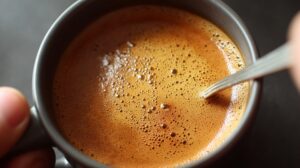 Close-up of a cup of coffee with a golden, foamy crema being stirred with a spoon