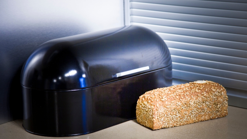 Loaf of bread next to a bread box on a counter to store bread at room temperature