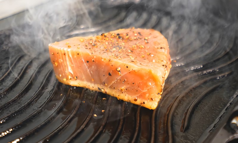A seasoned tuna steak with peppercorns sizzles on a grill