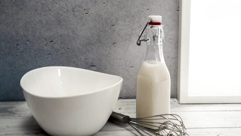 Glass bottle of sour milk next to a mixing bowl and whisk on a kitchen counter