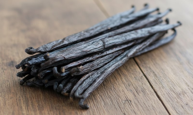 A bundle of dried, dark brown vanilla beans is arranged on a wooden surface