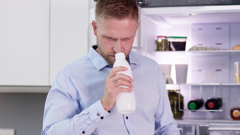 Man smells a bottle of milk and reacts to signs of spoilage