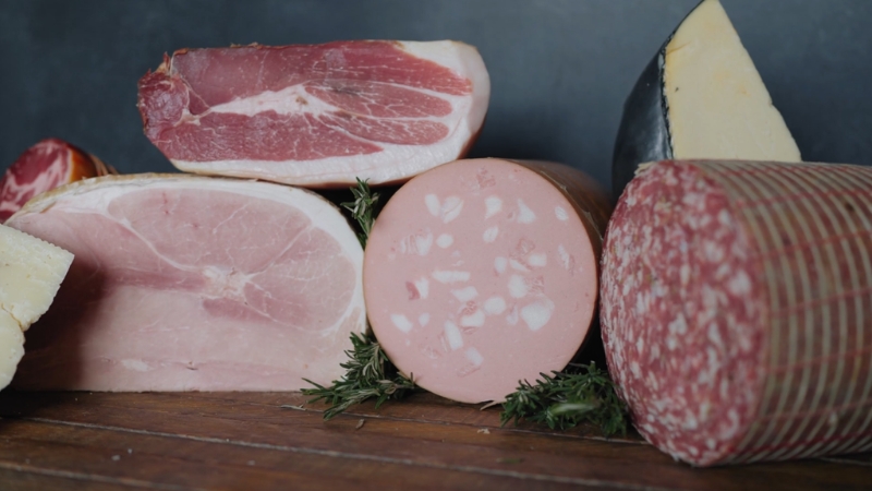 Assorted sliced deli meat and cured meats placed on a wooden surface