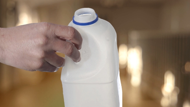 Hand holds a milk jug near the fridge showing concern about drinking sour milk