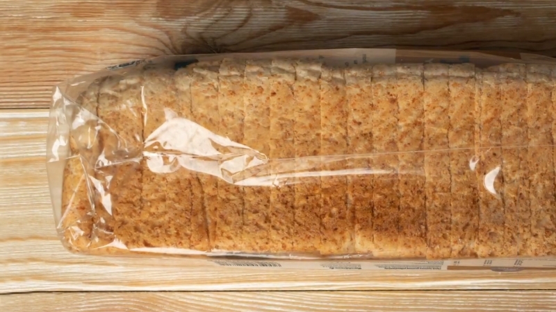 Sliced loaf of bread sealed inside a plastic bag on a wooden surface
