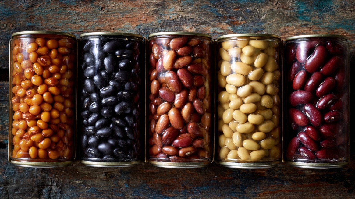 Five glass jars filled with different canned beans arranged side by side on a rustic surface