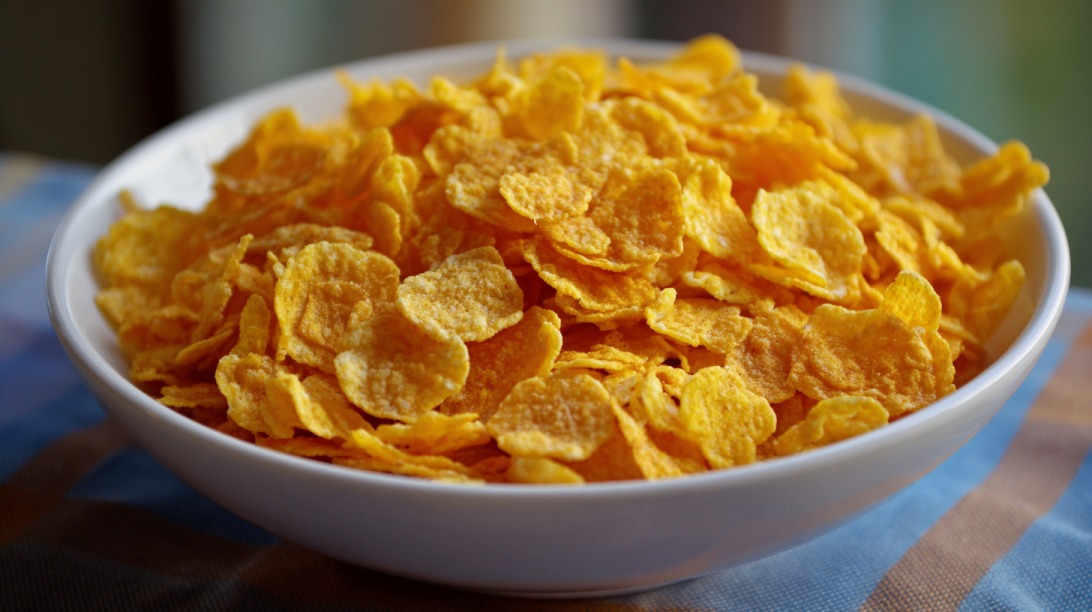 White bowl filled with golden corn flakes sitting on a table with a cloth underneath
