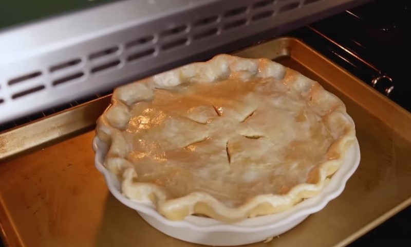 Golden-crusted pie with steam slits, baking in an oven on a metal tray