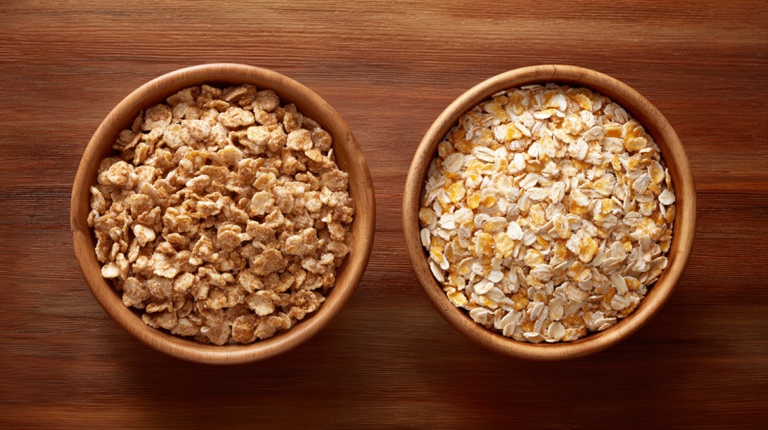 Top view of two wooden bowls filled with different types of cereal flakes on a wooden surface