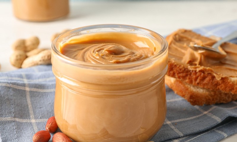 A jar of creamy peanut butter sits on a blue checkered cloth