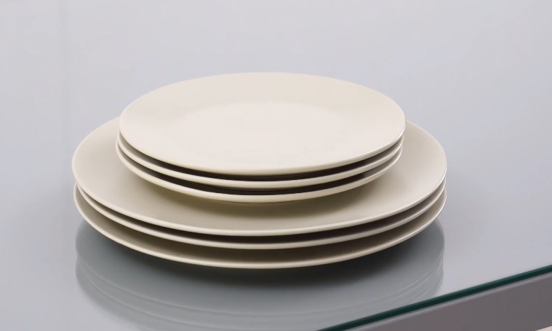 A stack of four white ceramic plates sit on a reflective glass surface