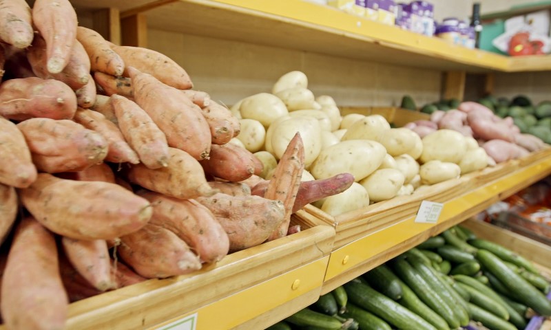 Assortment of fresh vegetables in a grocery store display. Sweet potatoes, regular potatoes, and cucumbers are neatly arranged on wooden shelves
