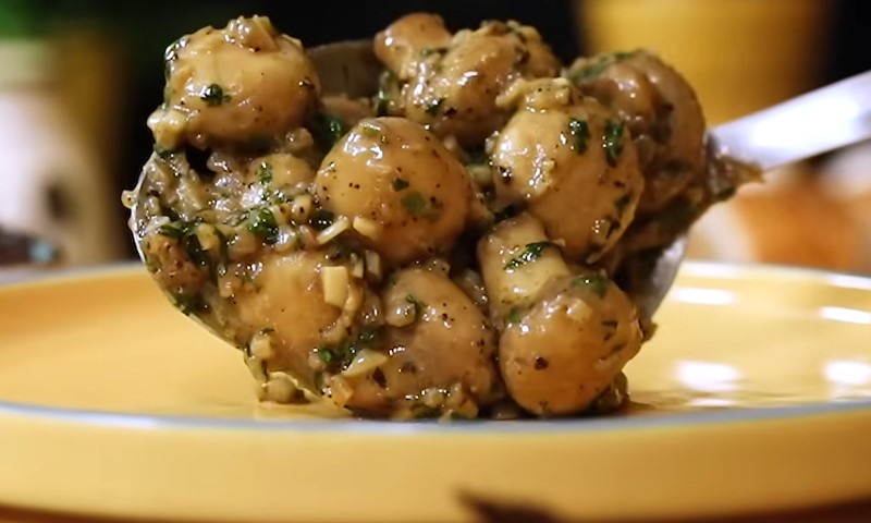 A spoonful of sautéed mushrooms with herbs and garlic is placed on a yellow plate
